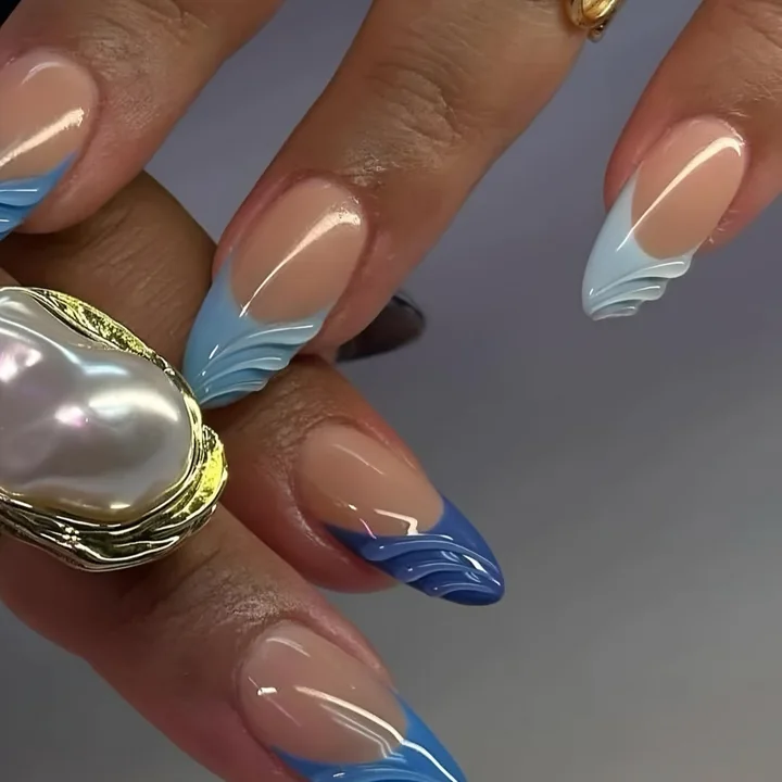 Almond nails with blue wave French tips, worn with pearl and gold rings