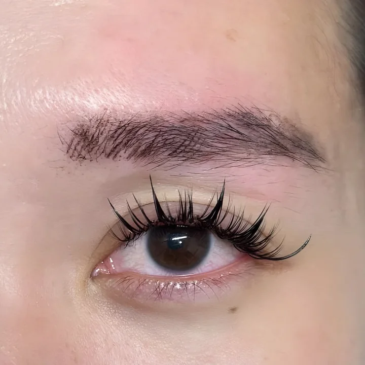 Close-up of a full brow above an eye with spiky wispy lash extensions