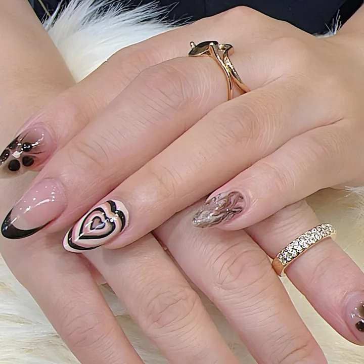 Nude almond nails with a brown heart swirl, black French tip and flower dots