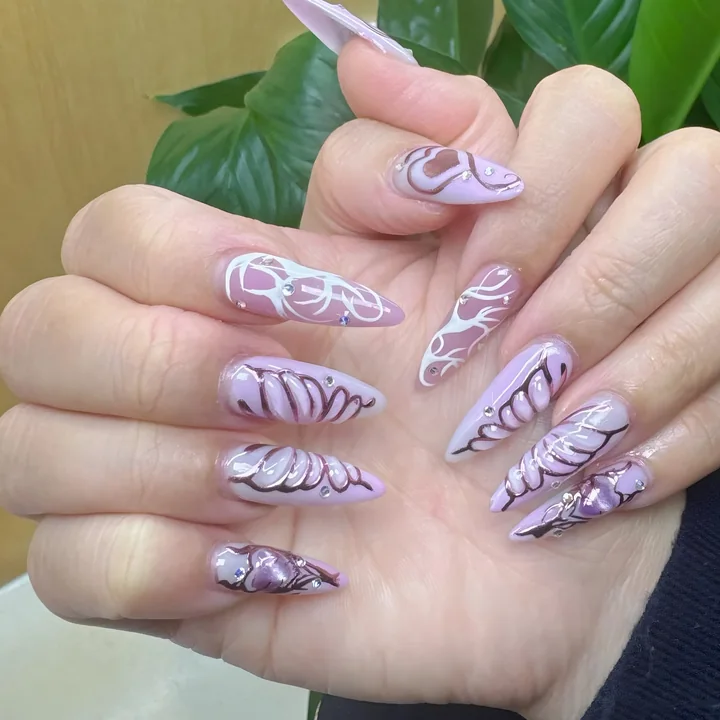 Long lilac stiletto nails with white and chrome swirl lines and small crystals