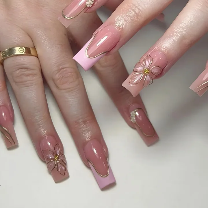 Long square nails in sheer pink with pink French tips, gold lines and a flower design